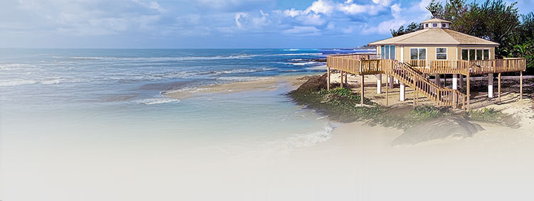Topsider octagon home elevated on pilings with a wraparound deck on the shoreline — post-and-beam structurally designed for coastal wind, flood exposure, and wide-open views.