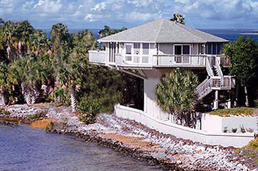 Topsider hurricane-resistant coastal Florida pedestal home surviving storm surge and waves during tropical storm or hurricane, elevated design for flood and wind protection with lush palm trees, oceanfront views, and sturdy construction.